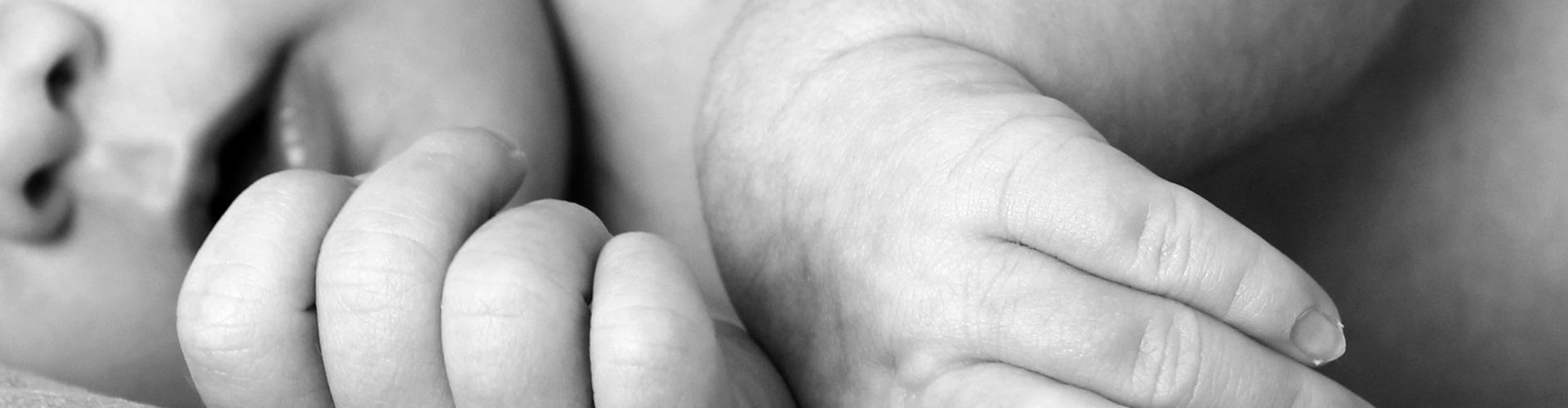 Black and white close-up of a newborn baby's hands, symbolizing innocence and new life.